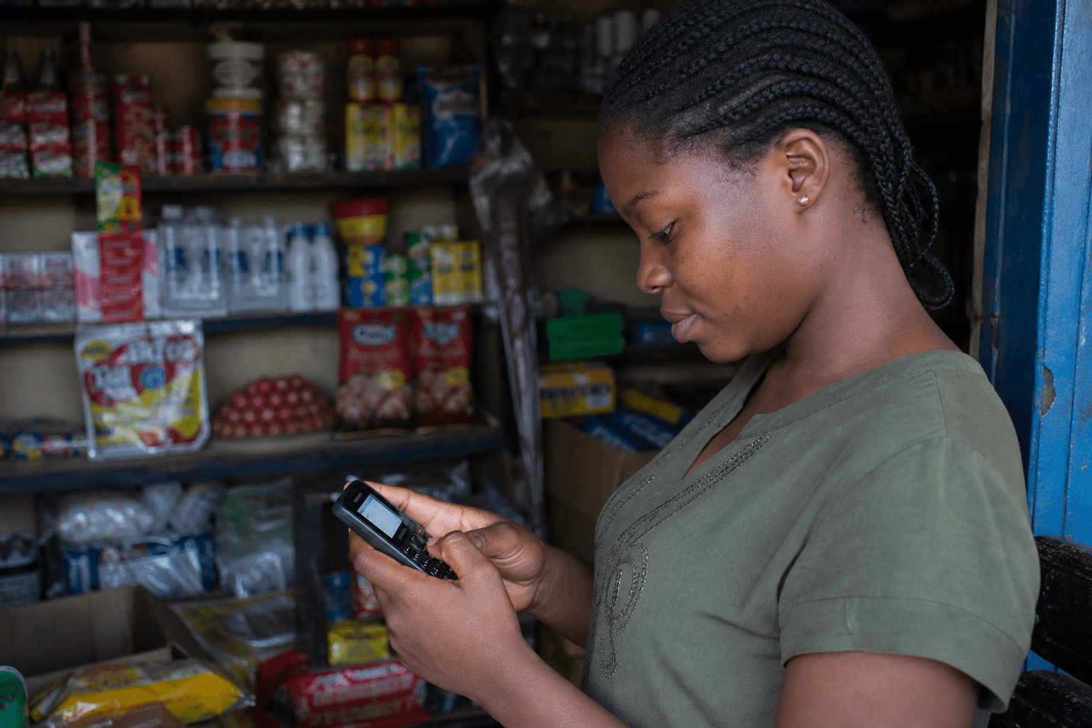 Young woman in a community store dialing a USSD code on a feature phone